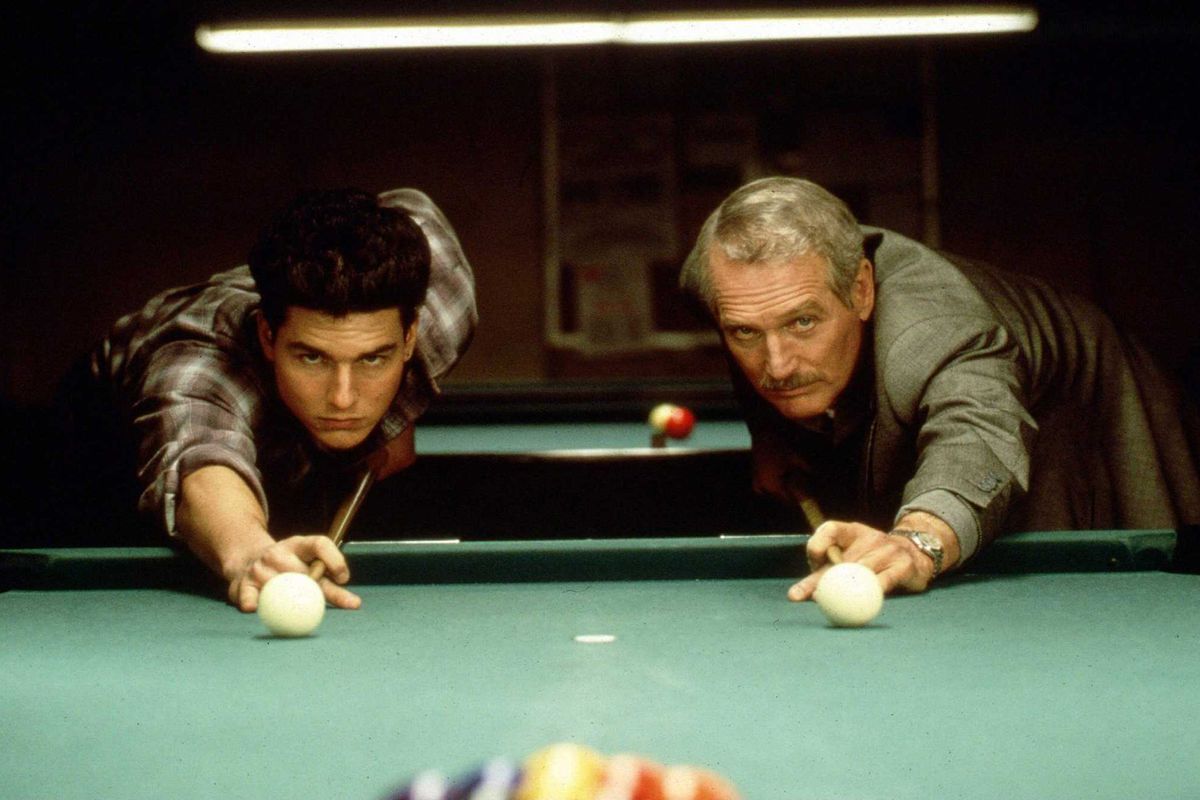 Two men shooting white pool hall balls at a pool table.