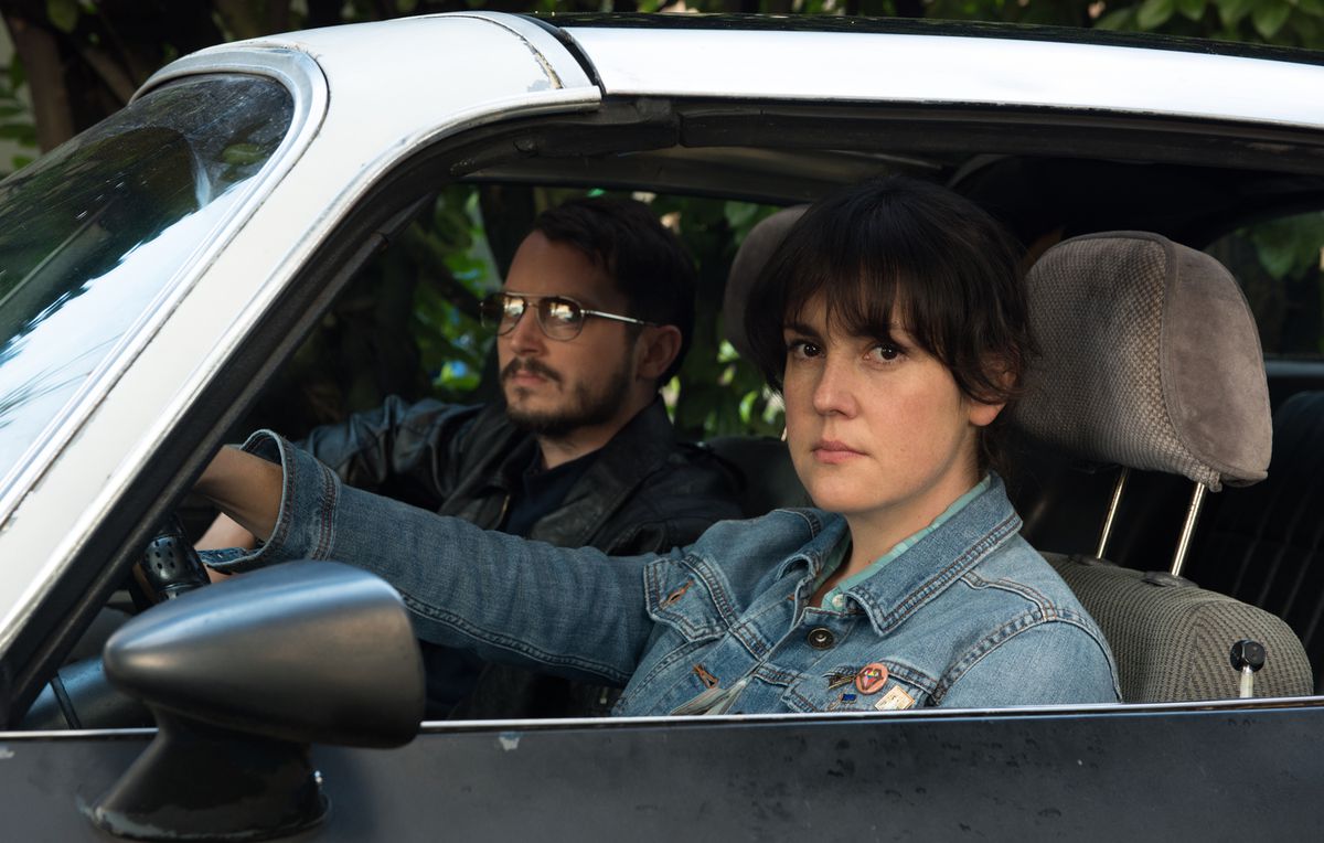 (LR) Elijah Wood and Melanie Lynskey sitting behind the wheel of a car in I don't feel at home in this world anymore