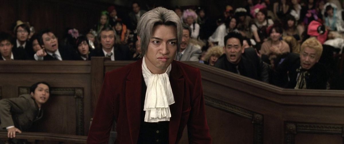 The crowd in the live-action adaptation of Ace Attorney responds by leaning in for a crucial moment, behind the scowling face of Miles Edgworth.