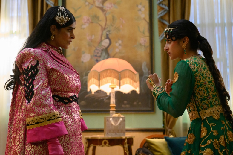 A teenage girl in bright green Pakistani evening dress raises her fists against a middle-aged woman in bright pink Pakistani evening dress;  more "Polite company"