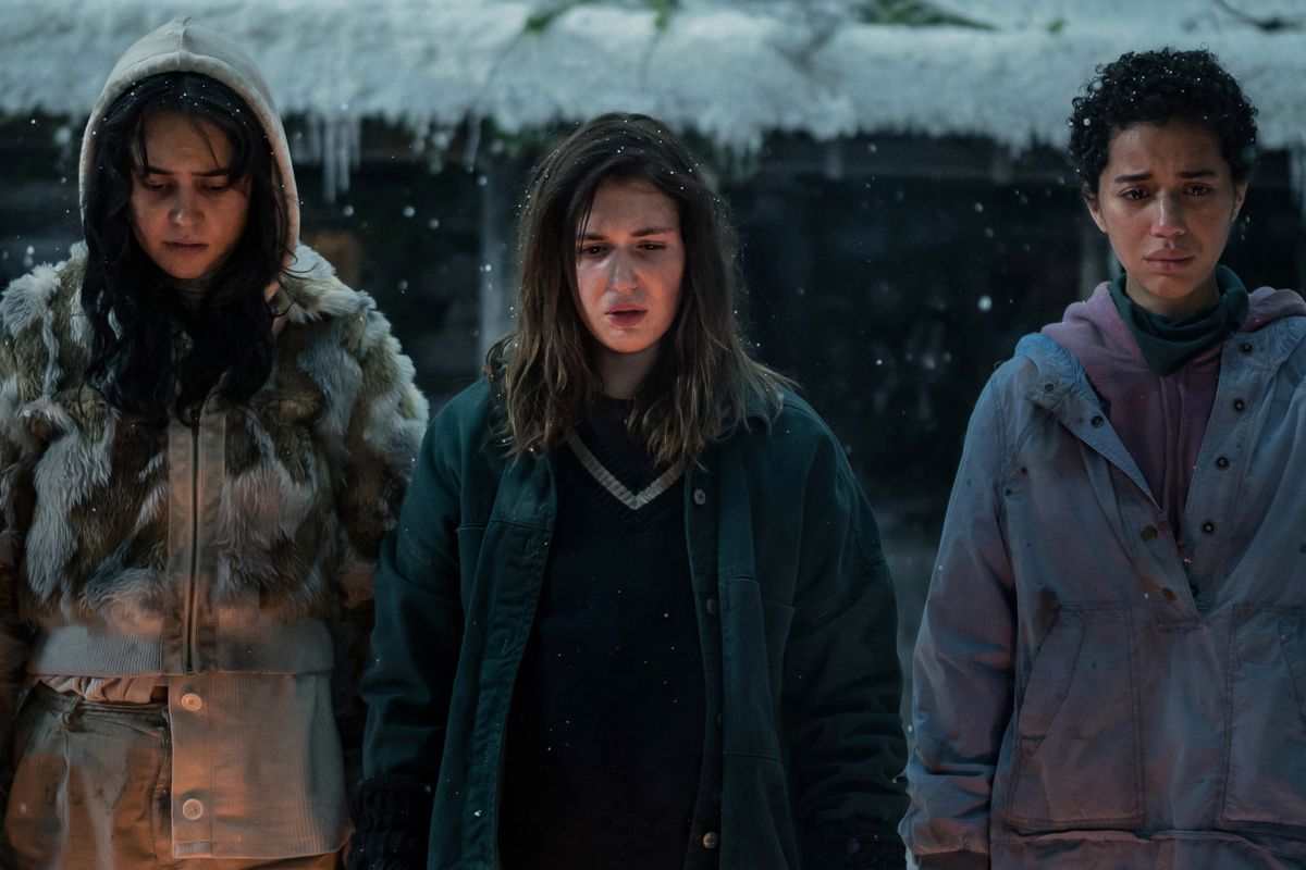 Lottie (Courtney Eaton), Shauna (Sophie Nélisse) and Tai (Jasmin Savoy Brown) stand and stare sadly at something in a photo from Season 2 of The Yellowjackets